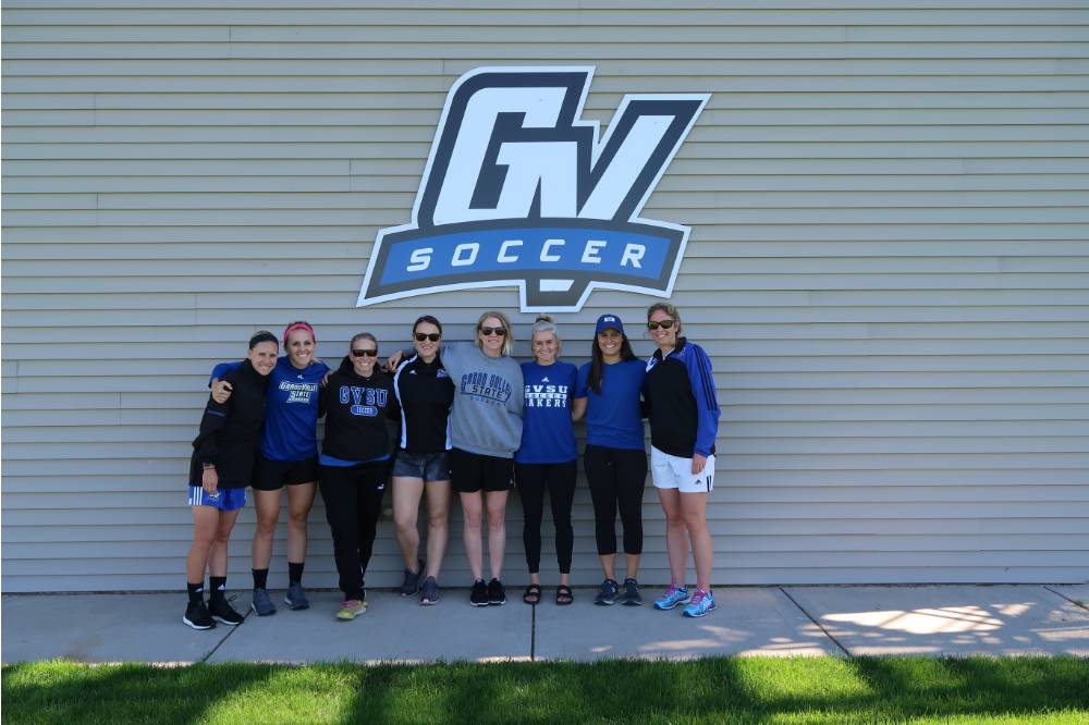 Alumni pose by the GV soccer wall